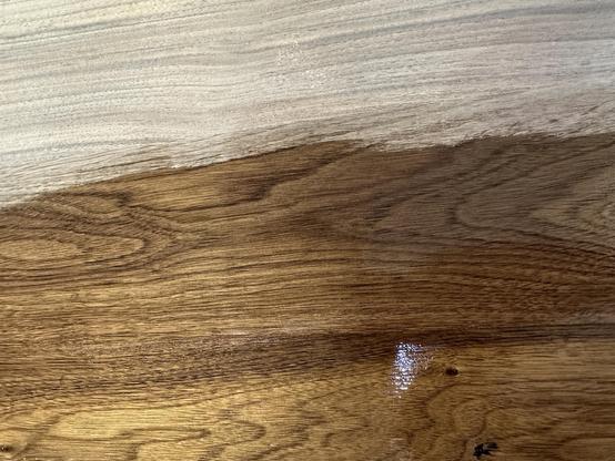 A close-up view of a wooden surface showing a contrast between two finishes: one side is a light, unfinished wood, while the other is a rich, dark-stained wood with a glossy sheen.