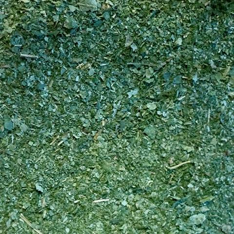 Close-up view of finely chopped dried green leaves, featuring varying shades of green and a texture that appears dry and crumbly. 