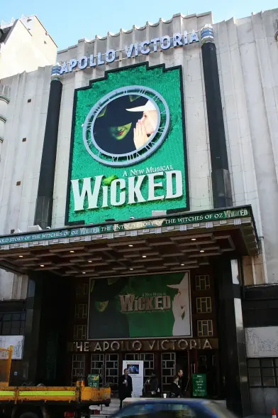 The image shows the exterior of the Apollo Victoria Theatre, which features a prominent advertisement for the musical "Wicked." The marquee displays the title, along with a visual element related to the show, giving it a vibrant and theatrical appearance. The building has an Art Deco architectural style.

Image Credits: Wikimedia / The Lud / Public domain
