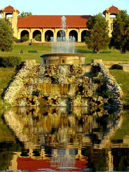 The image appears to show a scenic view of a fountain and waterfall surrounded by greenery, with a building in the background. The water reflects the fountain and the structure, creating a tranquil atmosphere. The setting seems to be a park or recreational area.

Image Credits: Wikimedia / Kris from Seattle, USA / CC BY 2.0