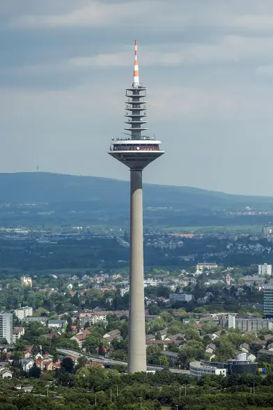 The image depicts a tall telecommunications tower. It features a cylindrical concrete base with antennas and a broadcasting area at the top, characterized by a distinctive design. Surrounding the tower are green areas and buildings, indicating it is situated in an urban or suburban environment. The sky appears partly cloudy. This type of structure is typically used for radio, television broadcasting, and telecommunications.

Image Credits: Wikimedia / Mylius / GFDL 1.2