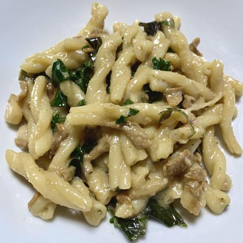 A bowl of pasta featuring twisted shapes mixed with greens and small pieces of mushroom, coated in a creamy sauce.