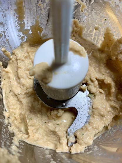 A close-up view of blended mixture inside a food processor, showing a creamy texture with light salmon color and a metal blade in the center.