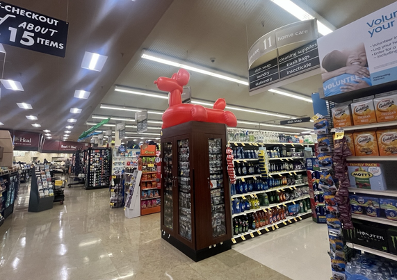 A large red vinyl blow-up in the style of a balloon animal atop an endcap in a grocery store. It has the poster of the Sphinx and a price tag of $39.99. 