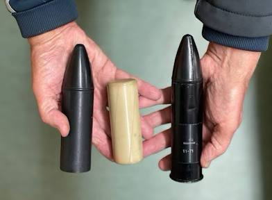 Two dildo-sized rubber bullets and one the size of a salt shaker, held in a man's hands. 