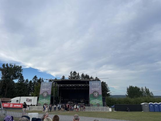 Under huge, fluffy clouds is an outdoor concert stage.