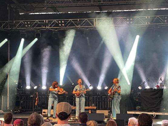 Sara on fiddle, Sarah on mandolin, and Aoife on guitar singing and playing on an outdoor stage.