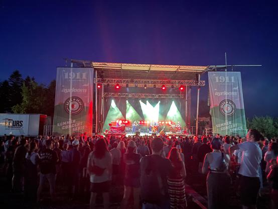 An outdoor concert stage lit up with red and green spotlights and surrounded by concert-goers.