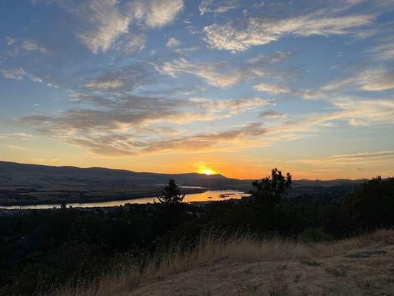 The sun rises, spreading golden hues across clouds above a winding river.