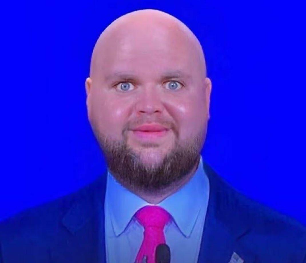 Portrait of a shiny bald. rotund JD Vance wearing what appears to be bright pink lipstick