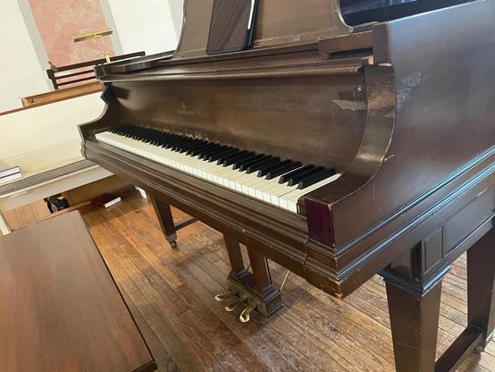 The keyboard of a Steinway grand piano with pedals below the keys, wood music stand above, and piano bench to the left. There is an iPad on the music stand.