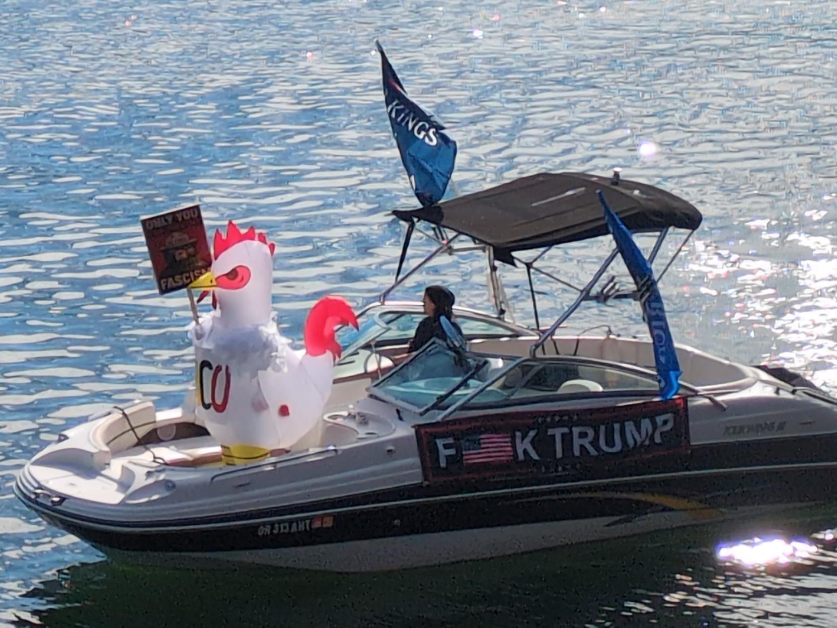 white chicken inflatable costume on boat on river, with sign F*CK TRUMP