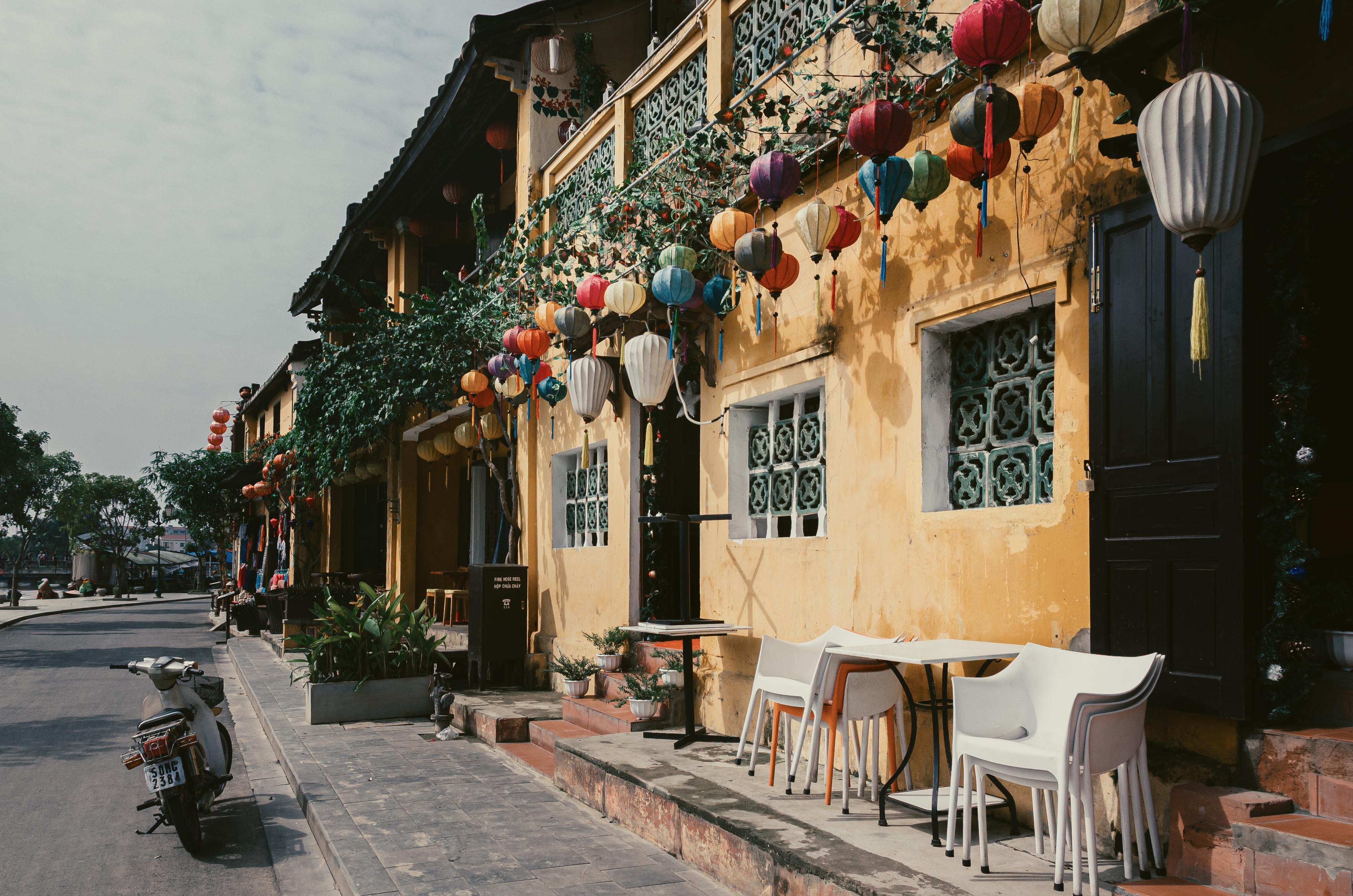 A street photograph in Hoi an, Vietnam. A traditional building with yellow painted walls and colourful lanterns is seen on the right, next to a street leading into the distance