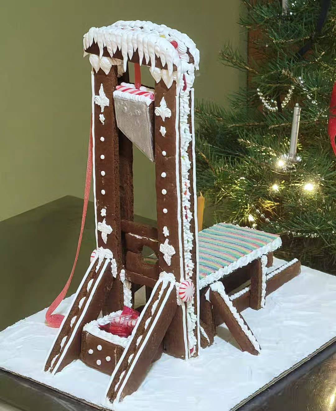 a gingerbread guillotine next to a Christmas tree.