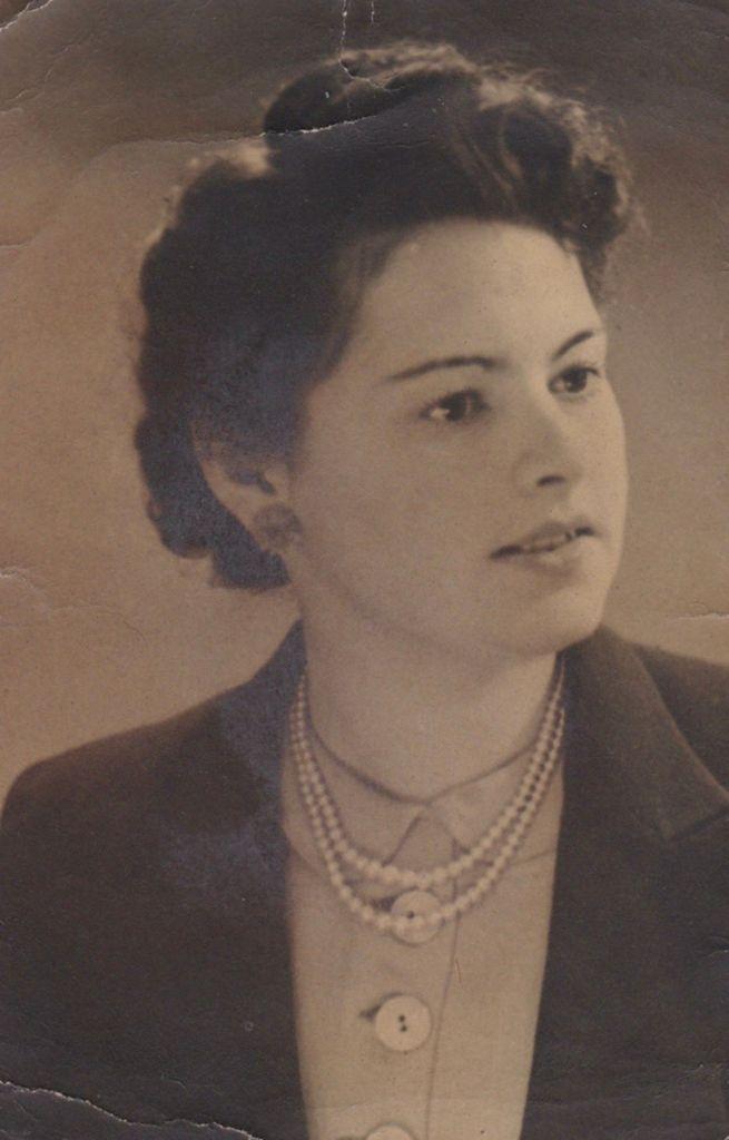 Vintage black-and-white portrait of a woman wearing a dark suit and pearl necklace, looking off to the side.