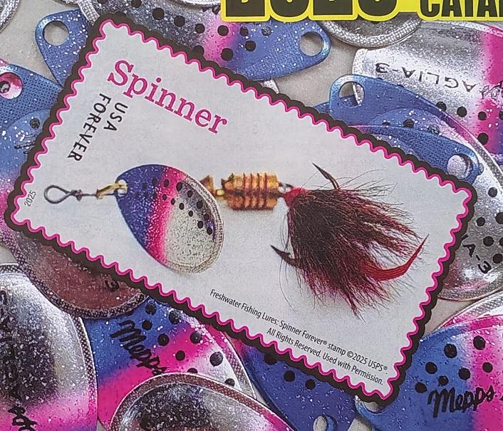 Rectangular postage stamp with an image of an in-line spinning lure. The lure has a blue, pink, and yellow blade, gold ribbed body, and dark brown stained squirrel hair.