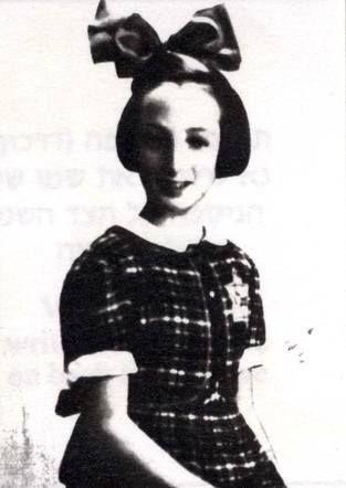 Black and white photo of a girl wearing a polka dot dress and a bow on the head, smiling at the camera.
