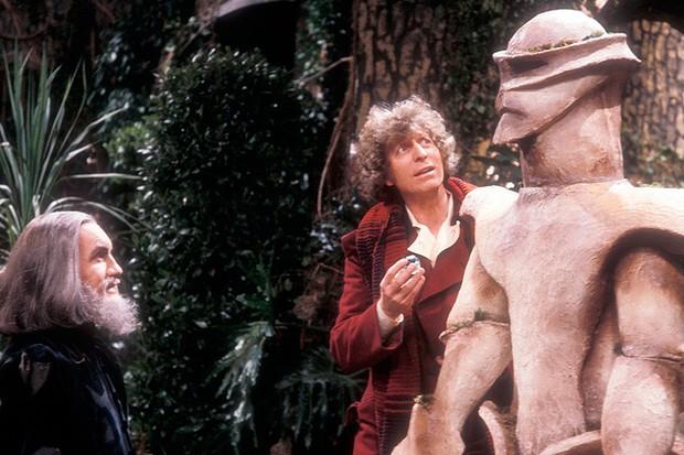 Tom Baker as the 4th Doctor standing next to the Melkur statue  in the Doctor Who story The Keeper of Traken.