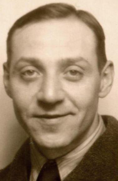 Black and white portrait of a smiling man wearing a suit jacket and collared shirt.