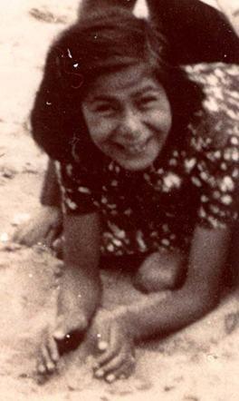 A vintage photograph of a smiling girl kneeling on a sandy surface, wearing a polka-dot top.