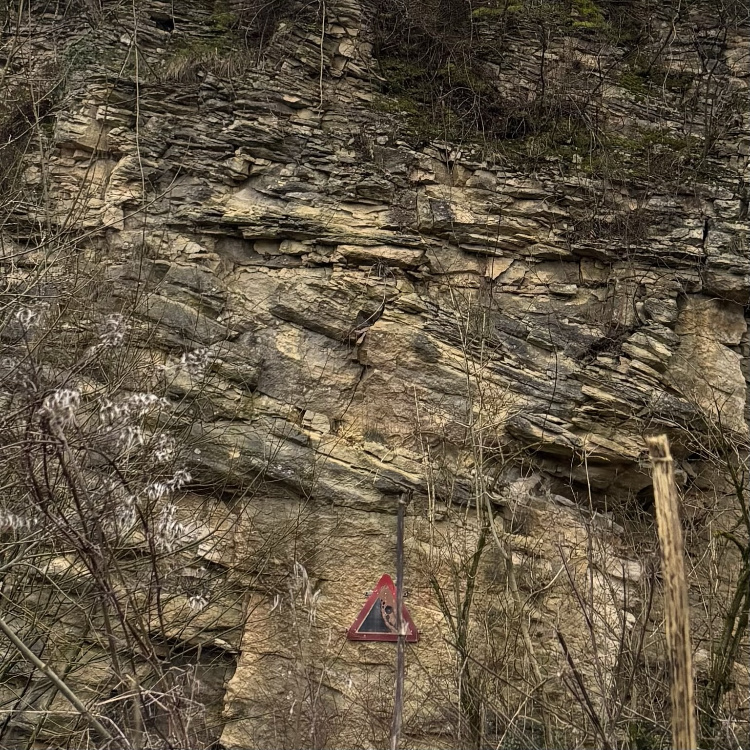 Limestone rock face with clear unconformity evident (tilted rocks uplifted and eroded with new deposition above). A sign warns of falling rocks