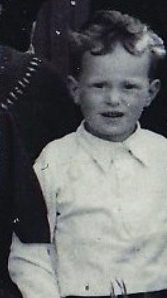 Vintage black and white photo of a young boy with curly hair, wearing a light-colored shirt.