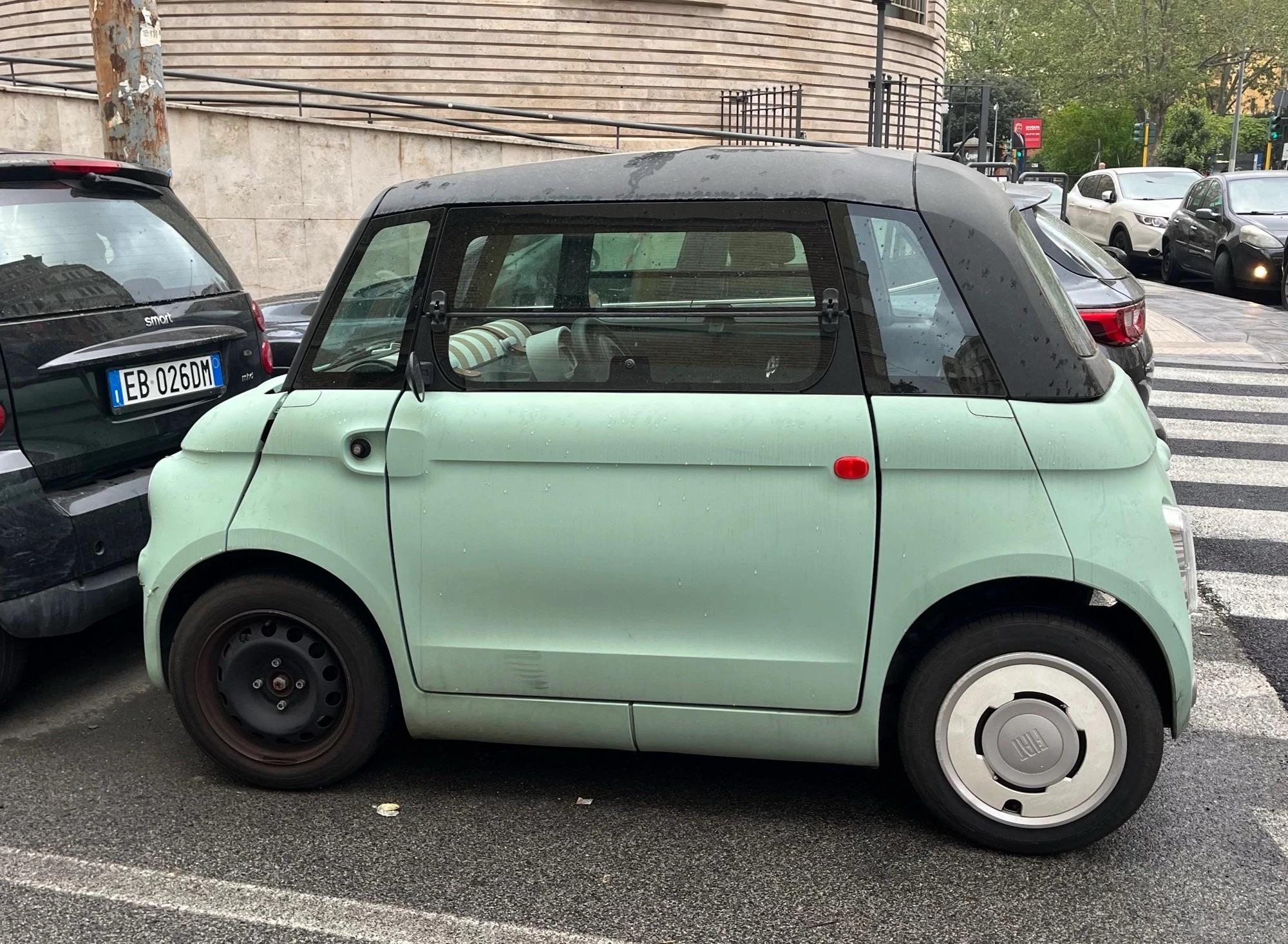 A compact, mint green electric car with a black roof parked on the street beside a larger black vehicle.