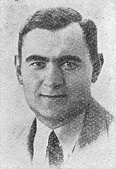 A blured portrait ID-style photo of a man in a suit. He has short dark hair.