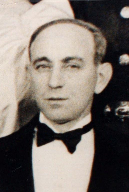 Photo of the face and shoulders of a man dressed in a tailcoat. He is wearing a bow tie under his neck. His hair is short.