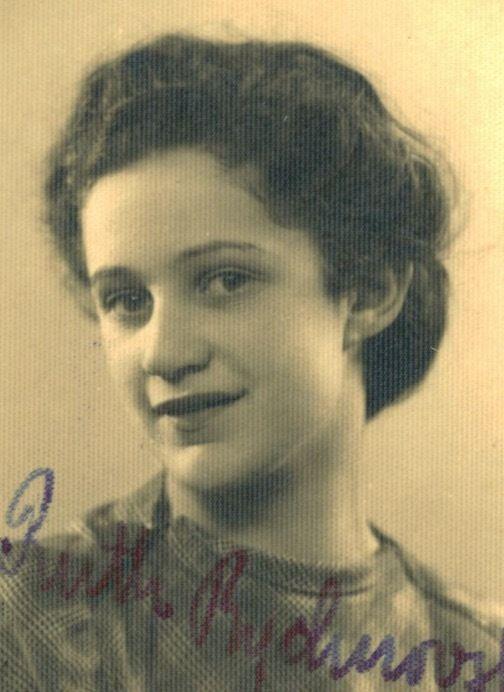 A portrait ID-style photo of a woman. The photo shows her handwritten signature. Her hair is lush and pinned back. Her ears are exposed. She is smiling slightly.