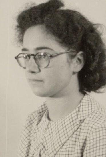 A picture of a girl's face with long, curled hair wearing glasses. She is wearing fine checkered clothing.