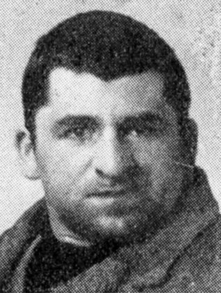 A photo of the face of a man with dark short hair. He is wearing a coat.