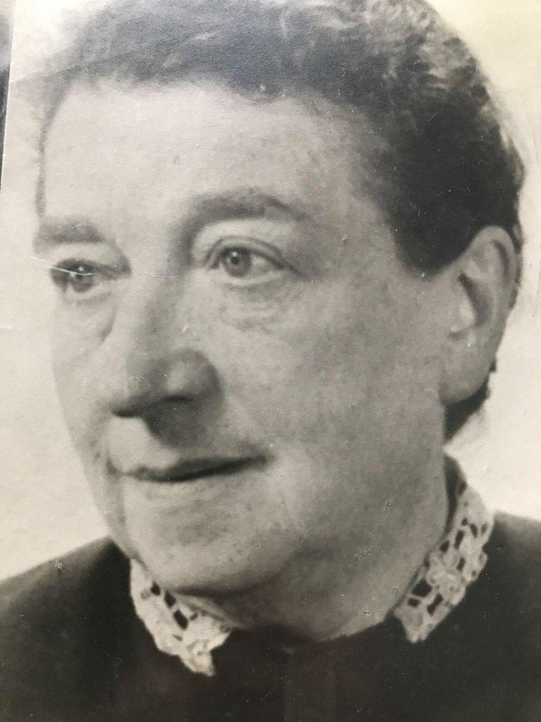 Black and white photo of an elderly woman with short hair, wearing a dark top with a lace collar, looking to the side.