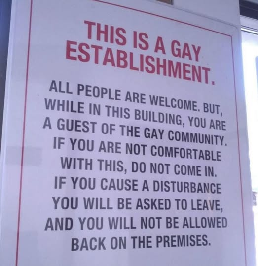 A close-up shot of a white sign with a red border, featuring text in all capital letters. The top heading is printed in bold red font, while the rest of the text is in bold black font.

The sign reads:
"THIS IS A GAY ESTABLISHMENT. ALL PEOPLE ARE WELCOME. BUT, WHILE IN THIS BUILDING, YOU ARE A GUEST OF THE GAY COMMUNITY. IF YOU ARE NOT COMFORTABLE WITH THIS, DO NOT COME IN. IF YOU CAUSE A DISTURBANCE YOU WILL BE ASKED TO LEAVE, AND YOU WILL NOT BE ALLOWED BACK ON THE PREMISES."