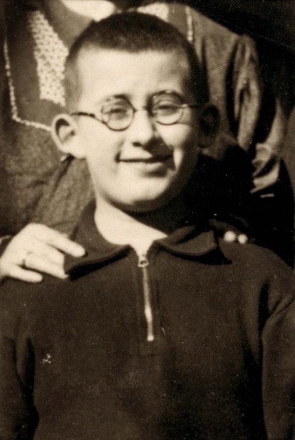 Vintage black-and-white photograph of a smiling young boy in glasses, wearing a zippered sweater.