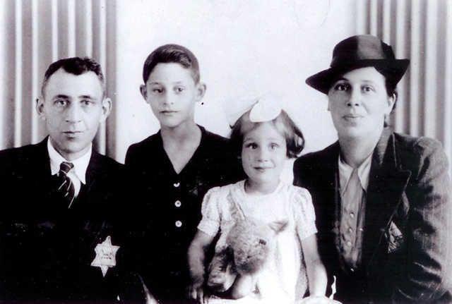 Black and white vintage photograph of four family members seated side by side. The person on the left is wearing a badge, next to a young person in a collared shirt, a child in a dress, and another adult in a hat.