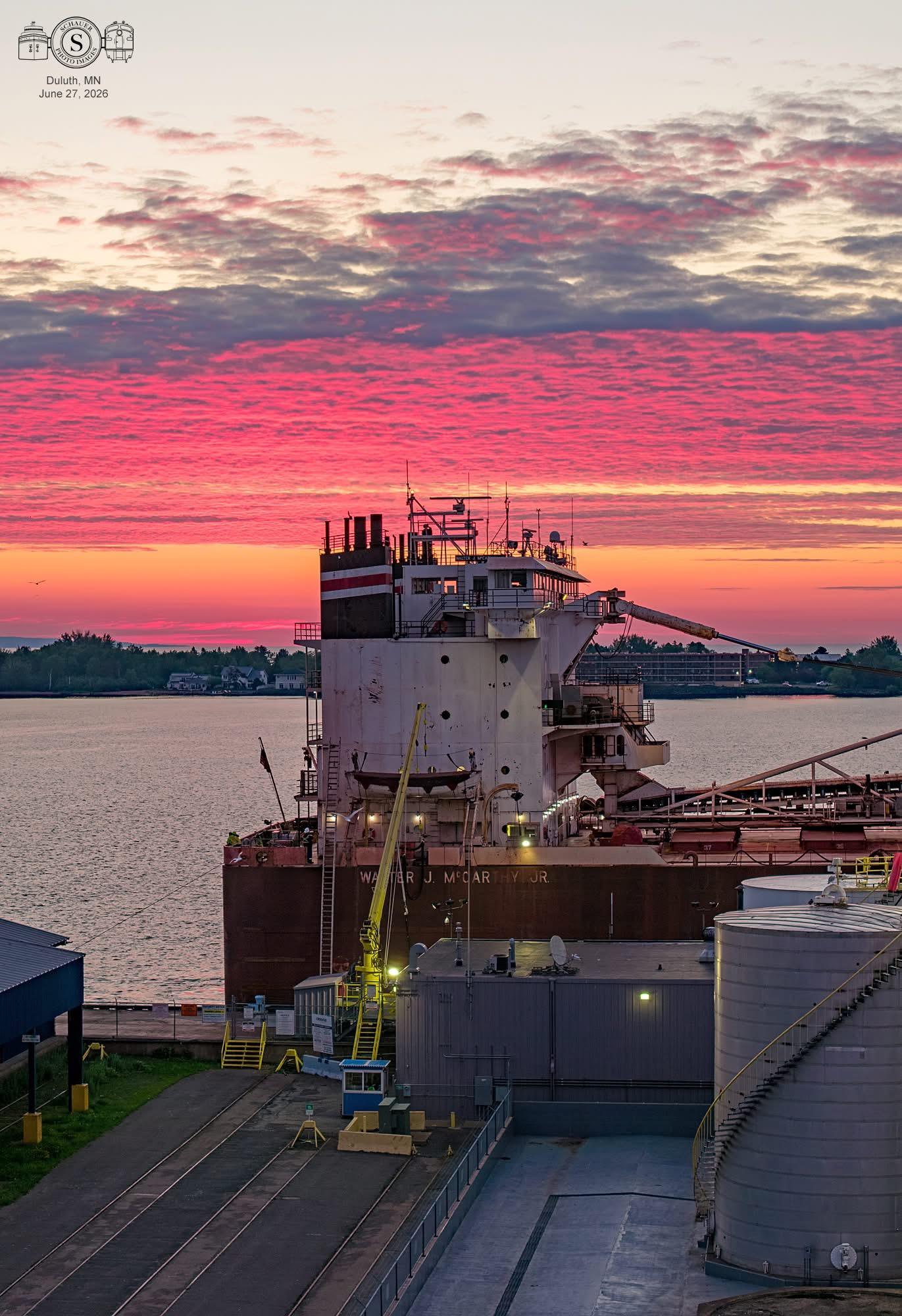 Photo of a Great Lakes freighter at a Duluth fuel dock with a colorful morning sky overhead.