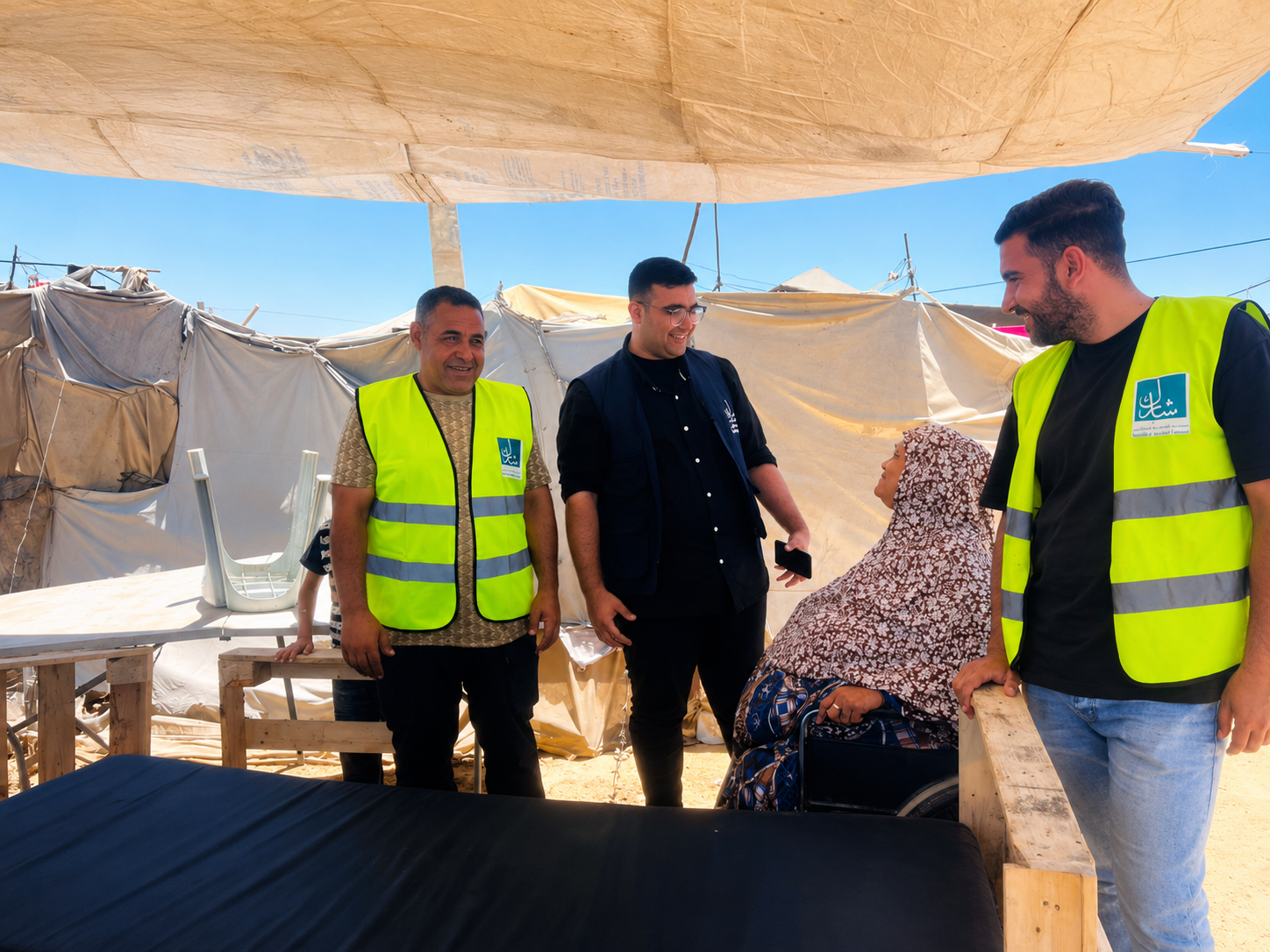 Field visit in Gaza with humanitarian workers speaking with a displaced woman inside a tent shelter.