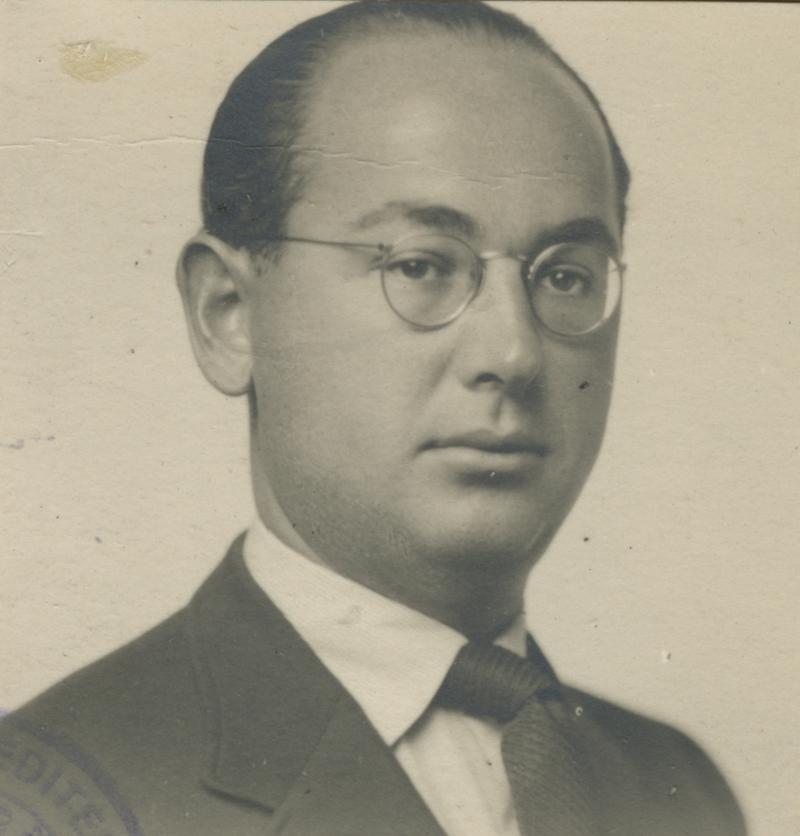 Vintage black-and-white portrait of a man wearing round glasses, a dark jacket, and a patterned tie.