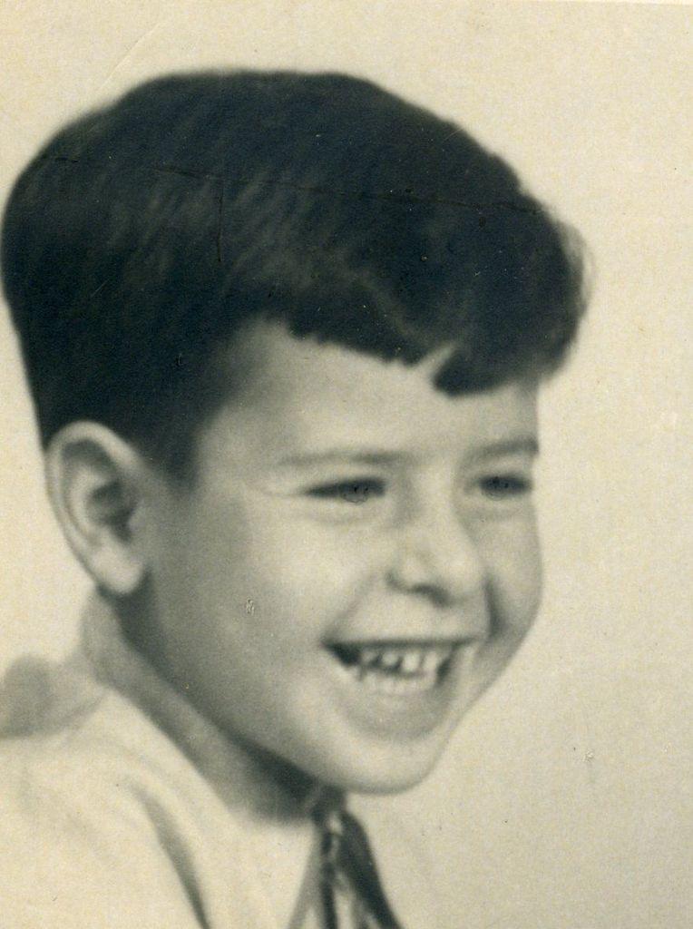 Vintage black-and-white portrait of a smiling boy with neatly combed hair, wearing a collared shirt and tie.
