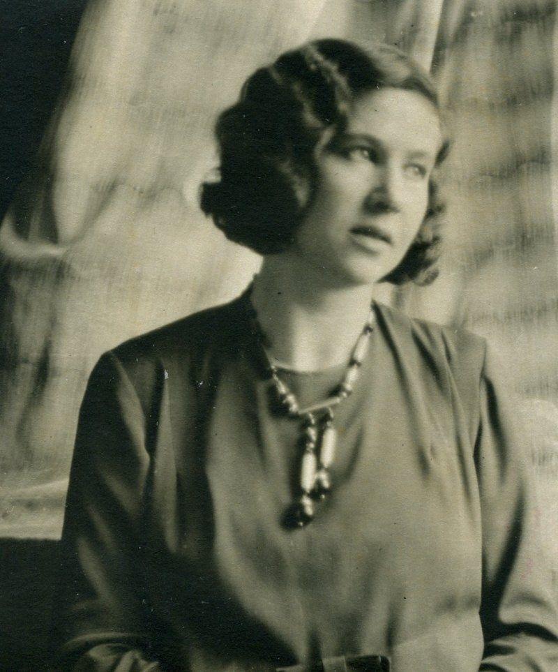 This is a vintage black-and-white portrait of a woman wearing a blouse with a rounded collar and adorned with a chunky necklace
