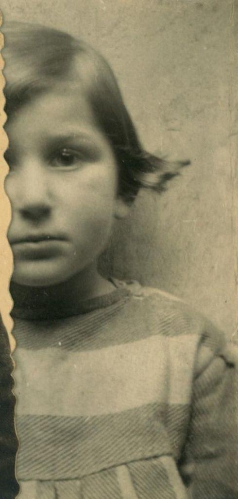 Old, torn black-and-white photograph of a young girl with tousled hair, wearing a striped shirt