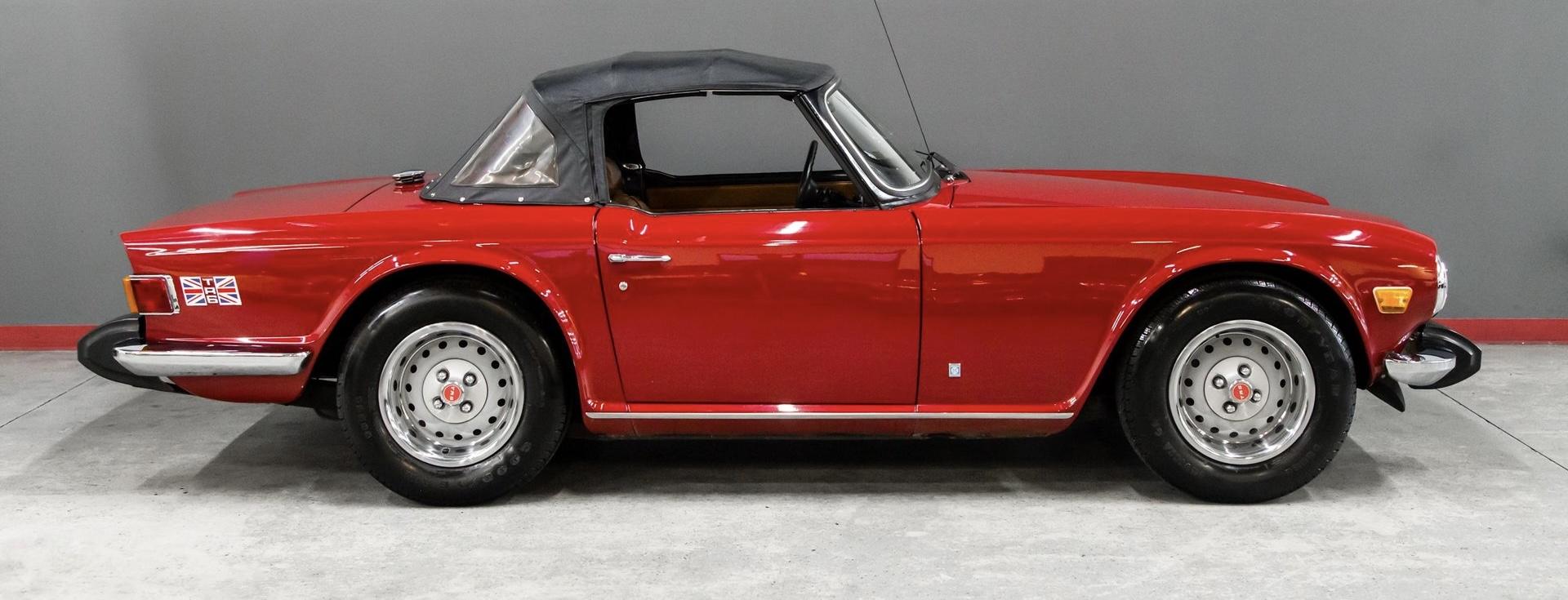 A photo of the side view of a red 1974 Triumph TR6 that has a British Union Jack near the exterior back of the vehicle