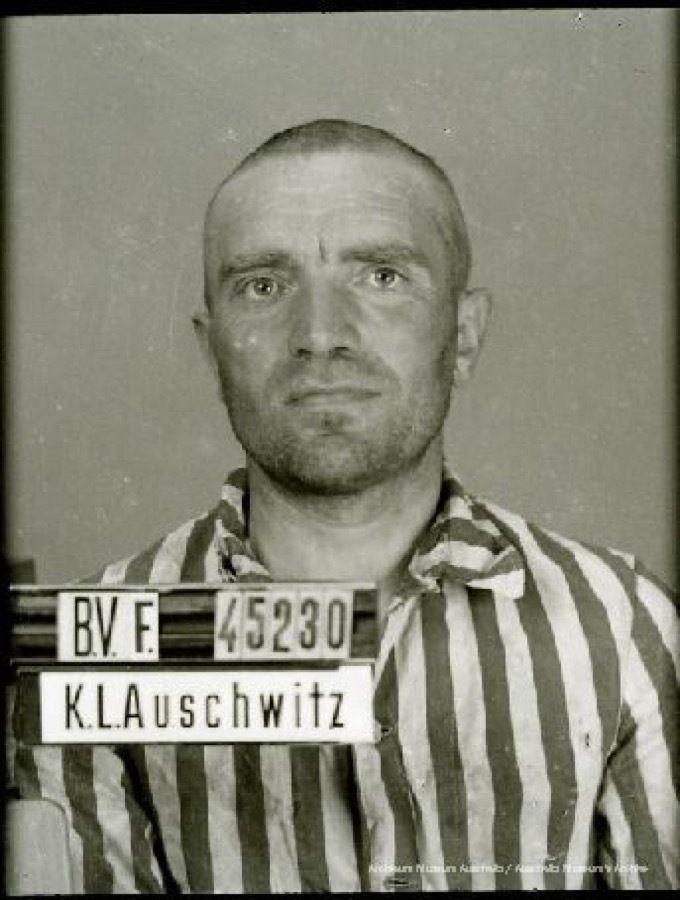 A mugshot registration photograph from Auschwitz. A man with a shaved head wearing a striped uniform