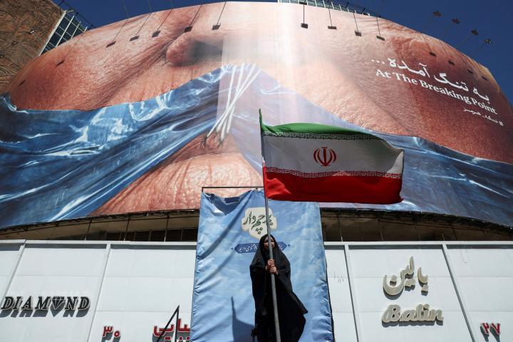 Una mujer sostiene una bandera iraní ant una valla antiestadounidense que muestra al presidente Donald Trump amordazado por el estrecho de Ormuz, en Teherán, el 25 de mayo de 2026. (Majid Asgaripour / WANA (West Asia News Agency) via REUTERS)