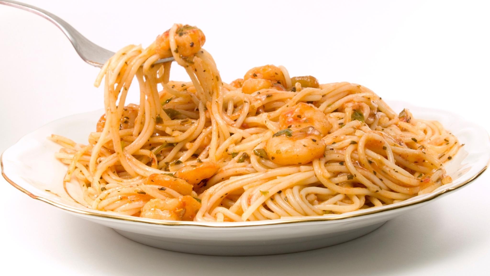 Fork twirling angel hair pasta in a shrimp sauce on a white rimmed plate.