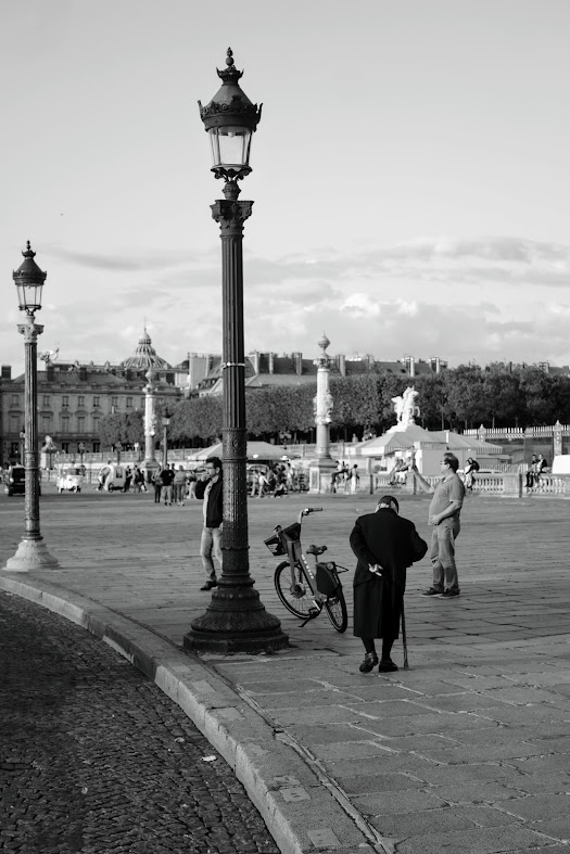 an old lady walking next a bike, a lamp post and two men.