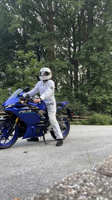 A stupid newbie rider in white riding gear and helmet perched upon his blue Yamaha R3 motorcycle trying desperately to look cool and sexy