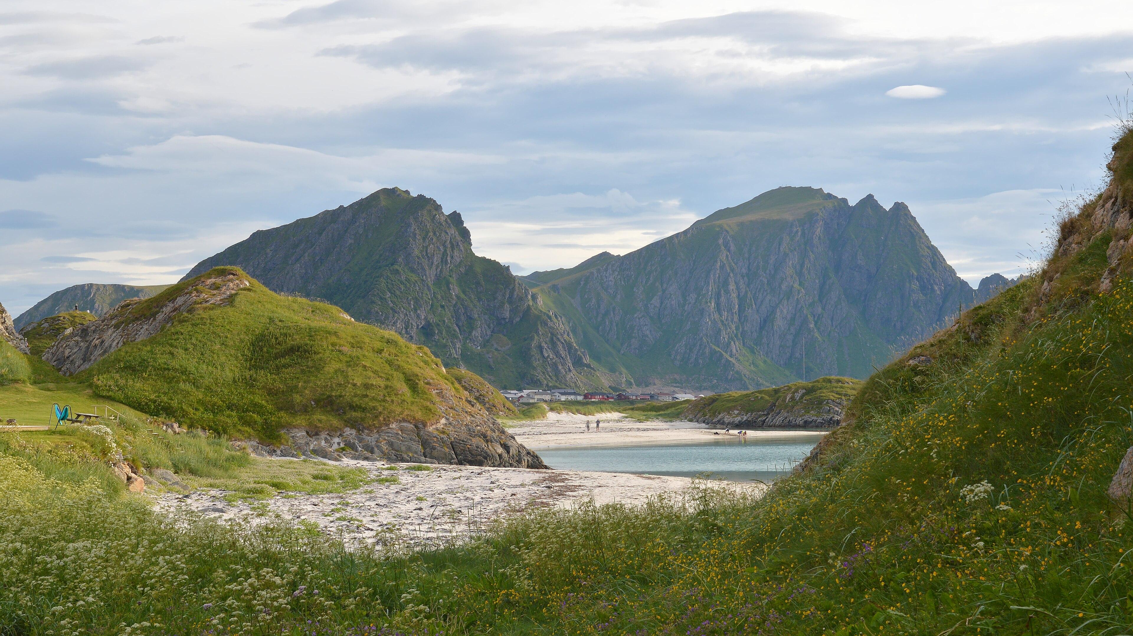 A photo of a sandy beach with jagged mountains in the distance. The sky is filled with clouds.