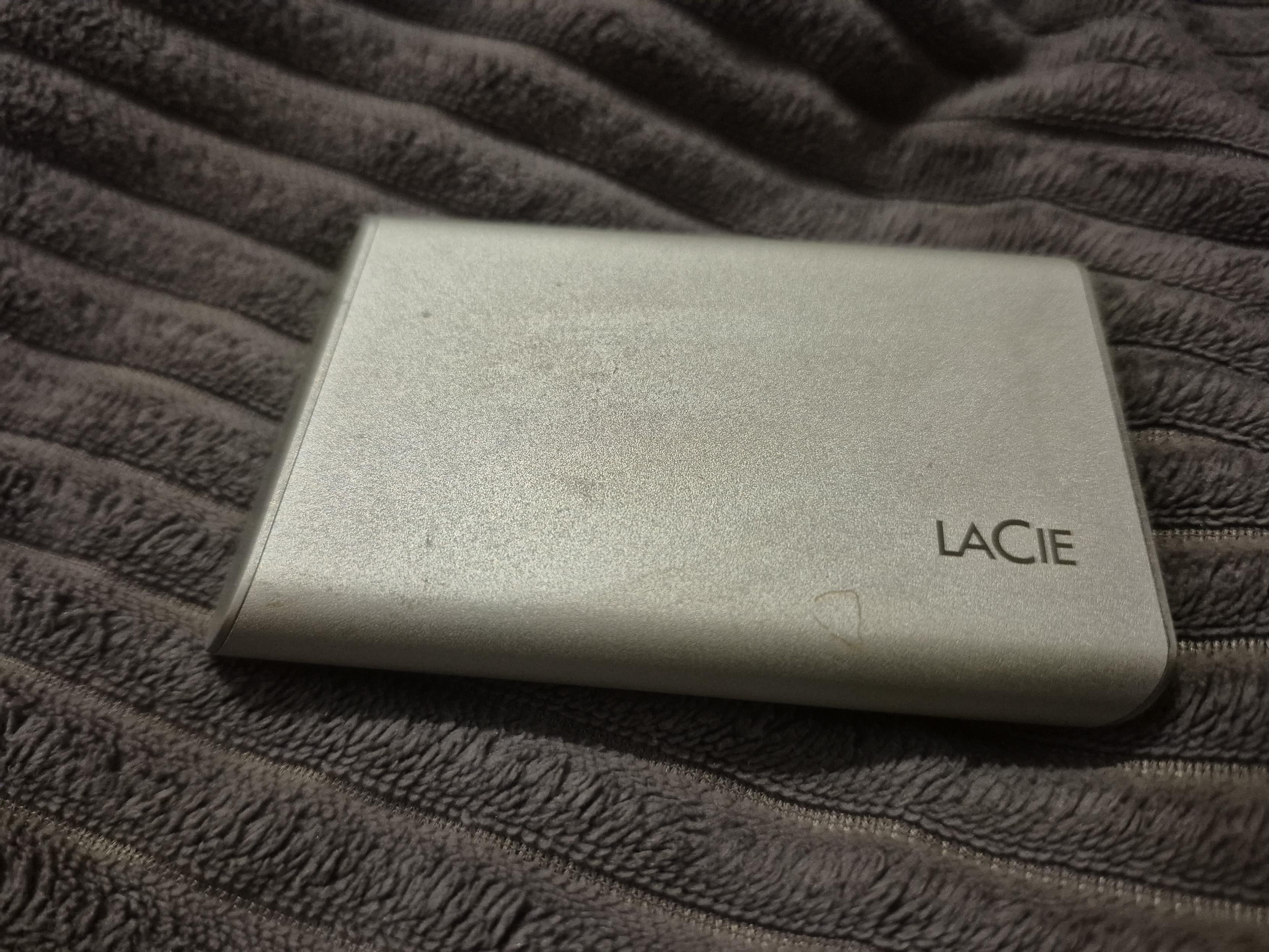 Silver LaCie portable external hard drive with light scuffs resting on a dark gray ribbed blanket.